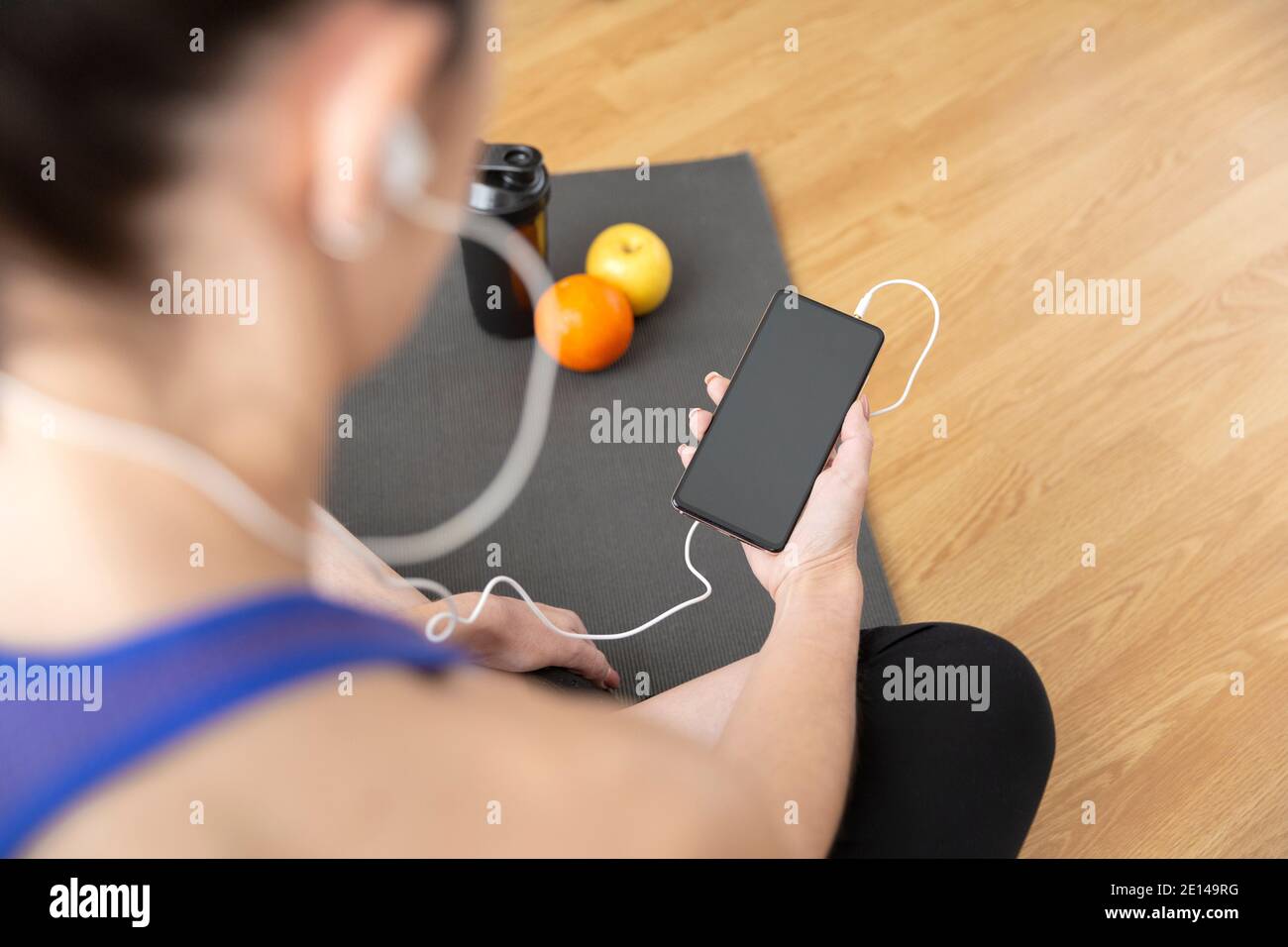 Gros plan sur une femme méconnaissable utilisant son smartphone tout en pratiquant du sport à la maison. Espace pour le texte. Banque D'Images