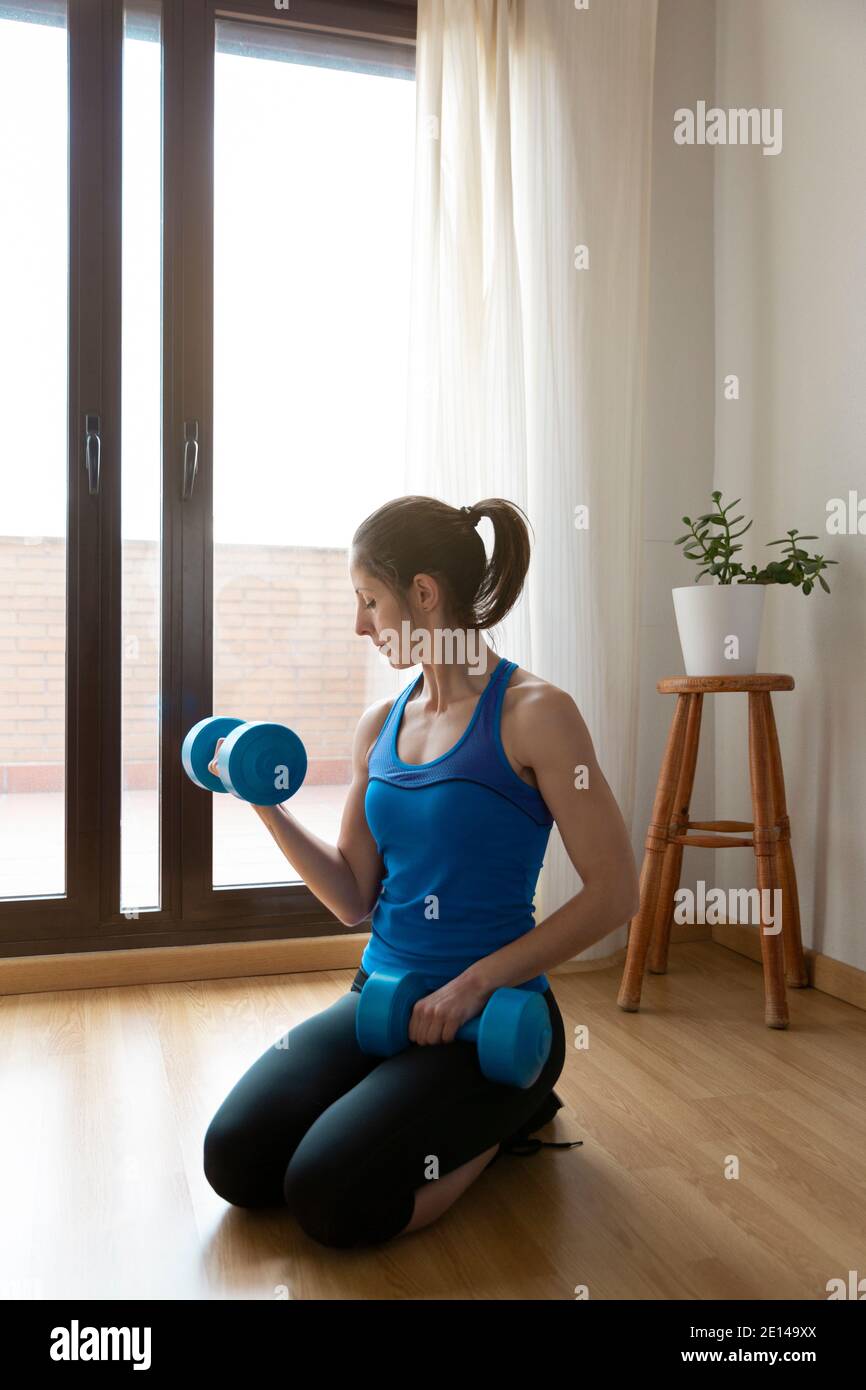 Femme exerçant ses muscles à l'aide d'une paire de haltères. Concept de sport à la maison. Espace pour le texte. Banque D'Images