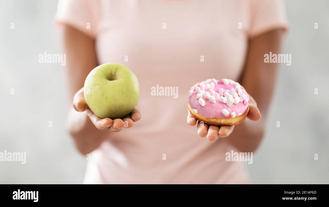 Choix de nourriture saine ou de la malbouffe. Gros plan de la femme noire qui choisit entre le beignet et la pomme sur un arrière-plan clair Banque D'Images