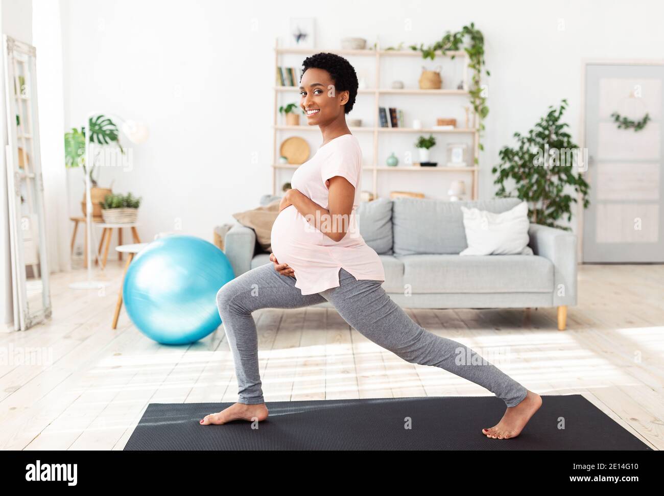 Grossesse active et sportive. Gaie femme noire enceinte faisant des fentes, étirant ses jambes, s'exerçant à la maison Banque D'Images