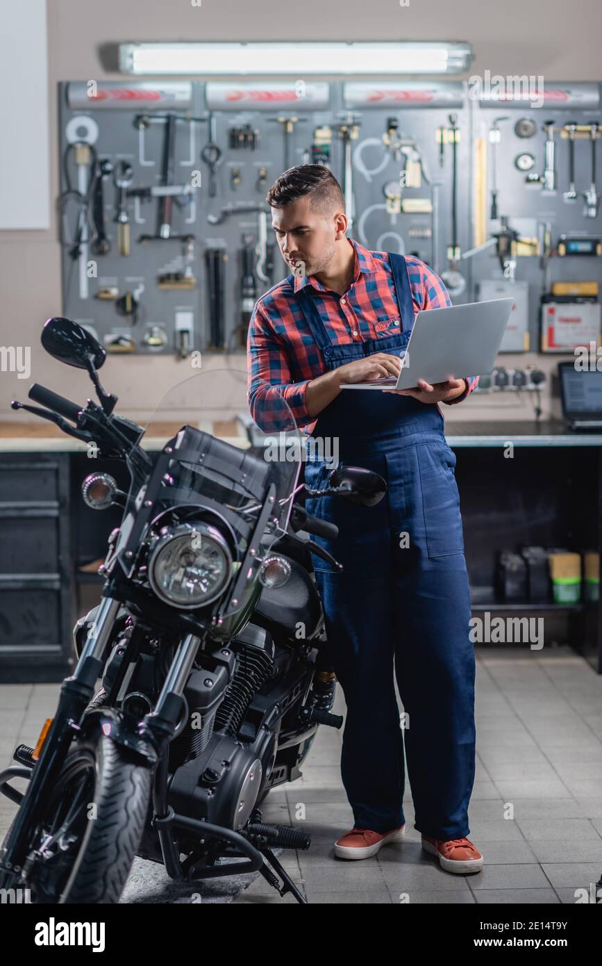 vue en longueur du mécanicien dans une combinaison avec un ordinateur portable à proximité moto dans le garage Banque D'Images