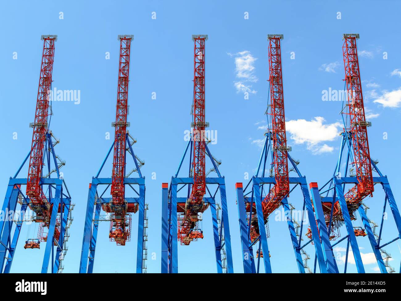 Cinq grues portiques à conteneurs peintes en rouge et bleu avec flèches verticales levées avant le ciel bleu dans le port de Hambourg, Allemagne Banque D'Images