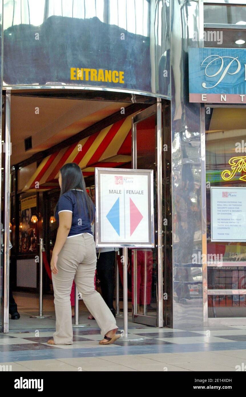 Un Filipina ignore le panneau d'entrée indiquant que les mâles entrent à gauche du panneau et les femelles à droite du panneau. Les normes culturelles concernant le traitement des sexes et le respect des règles se trouvent à l'entrée d'un magasin à Manille, aux Philippines. Banque D'Images