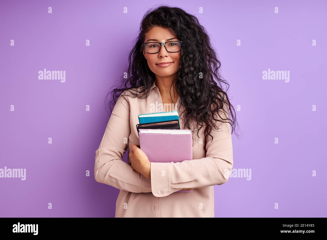 timide étudiante femme dans le stand de lunettes tenant des livres dans les mains et regardant la caméra, portant le chemisier. éducation, université Banque D'Images