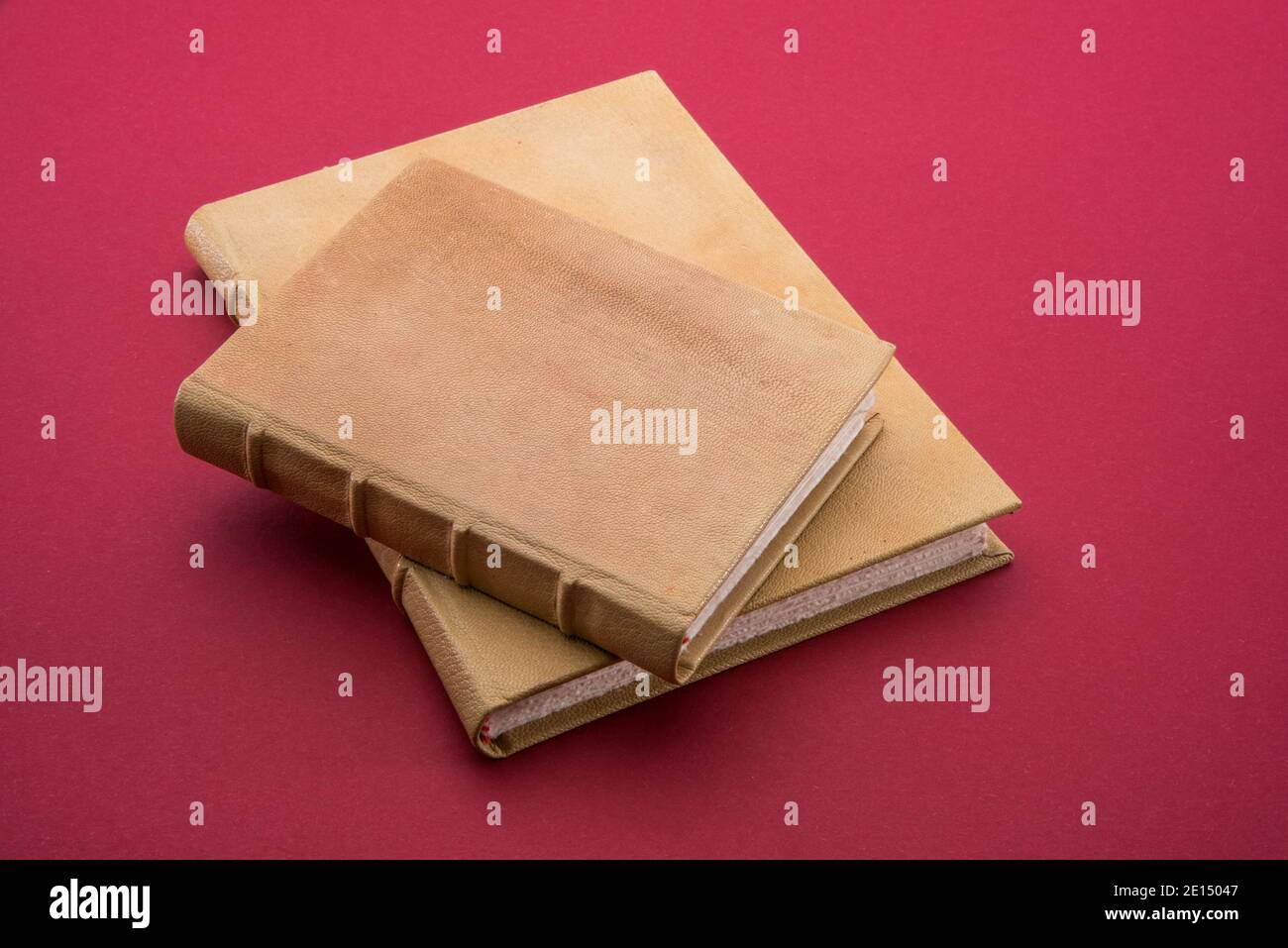 Deux livres anciens avec couverture rigide en cuir brun clair, un petit sur l'autre grand sur fond rouge cardinal Banque D'Images