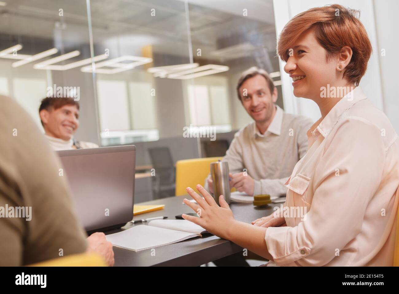 Une femme entrepreneure riant, discutant avec son équipe créative lors d'une réunion au bureau Banque D'Images