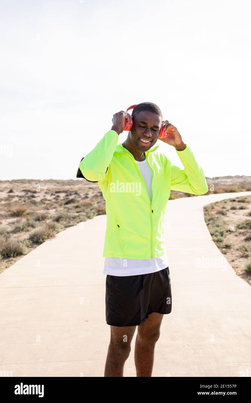Photo verticale d'un jeune coureur noir souriant dans une veste de pluie jaune qui aime écouter de la musique sur son téléphone portable avant ou après l'entraînement. Banque D'Images