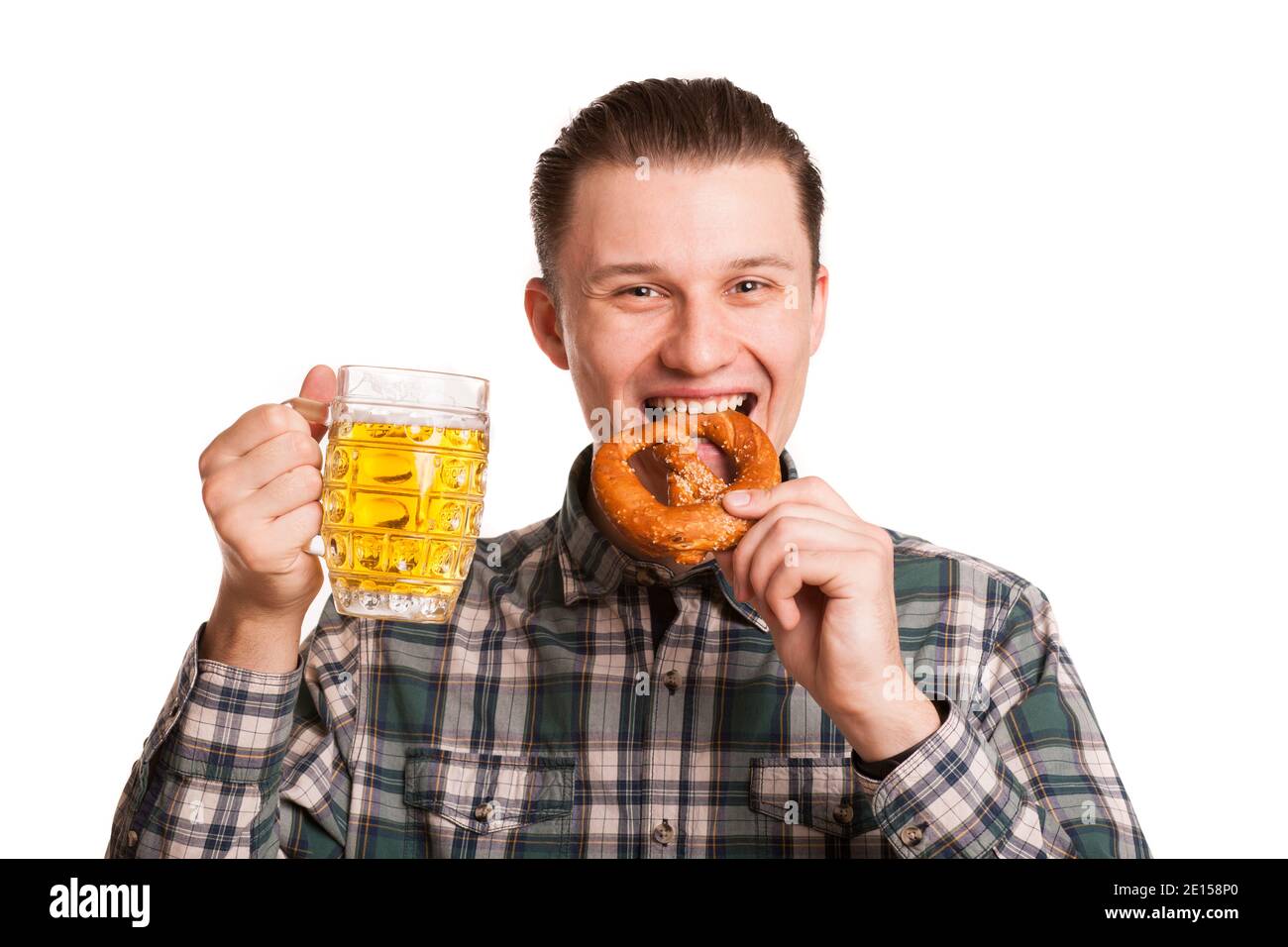 Un jeune homme joyeux qui apprécie de manger un bretzel délicieux, tenant un verre de bière dans la main tout en célébrant l'Oktoberfest. Bon homme à boire b Banque D'Images