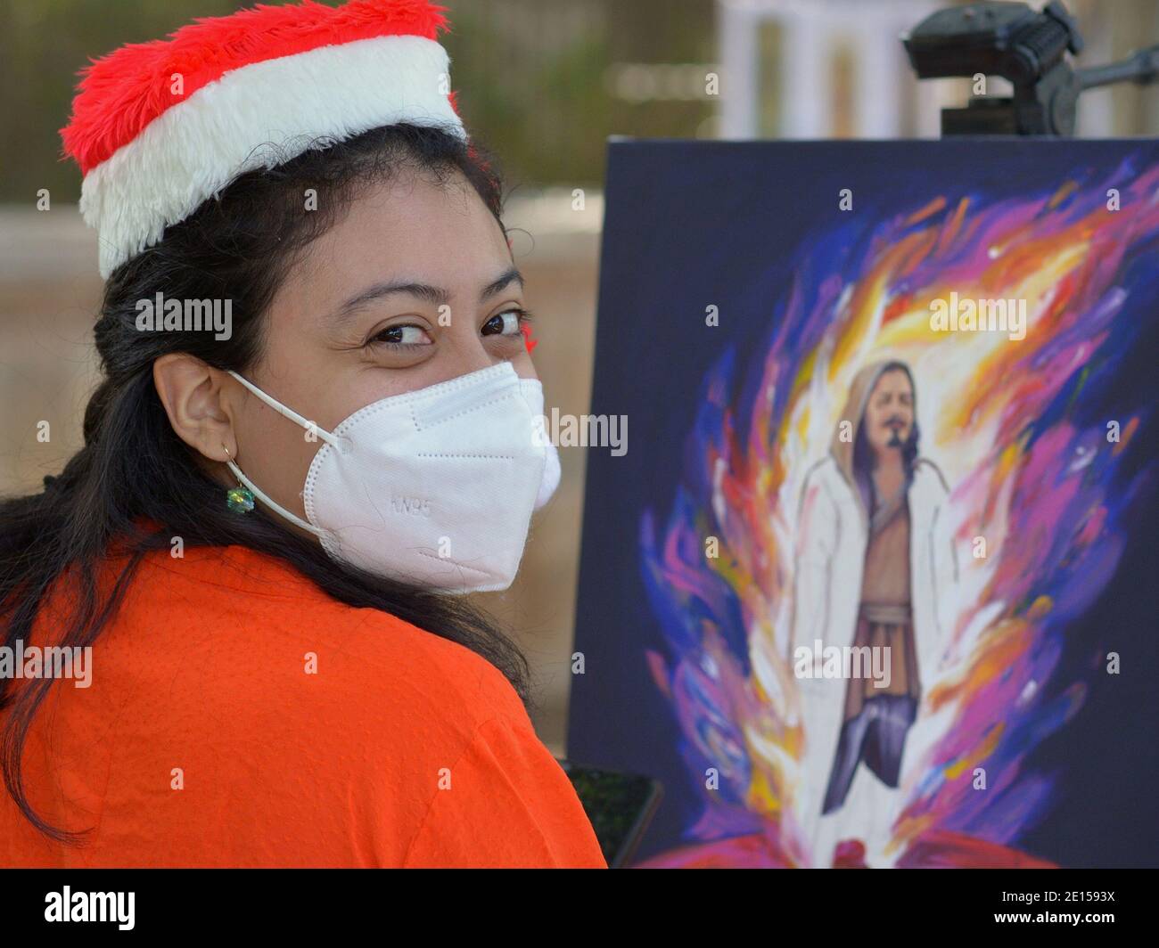 Beau jeune artiste peintre mexicain avec les yeux souriants porte un drôle chapeau de Père Noël et un masque KN95 pendant la pandémie mondiale de coronavirus. Banque D'Images