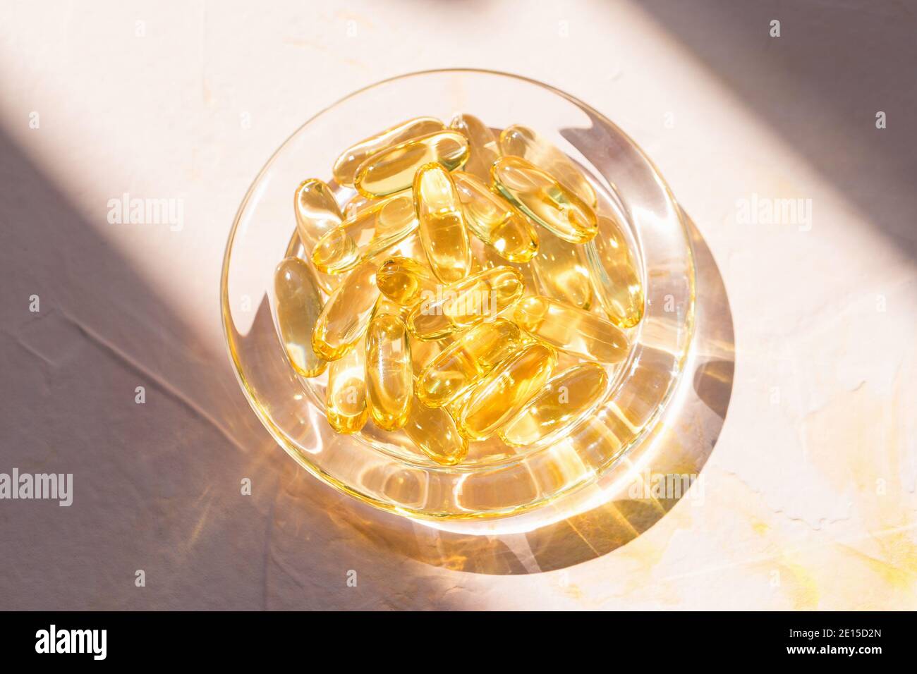 Capsules d'huile de poisson de foie de morue dans un bol en verre sur rose Banque D'Images