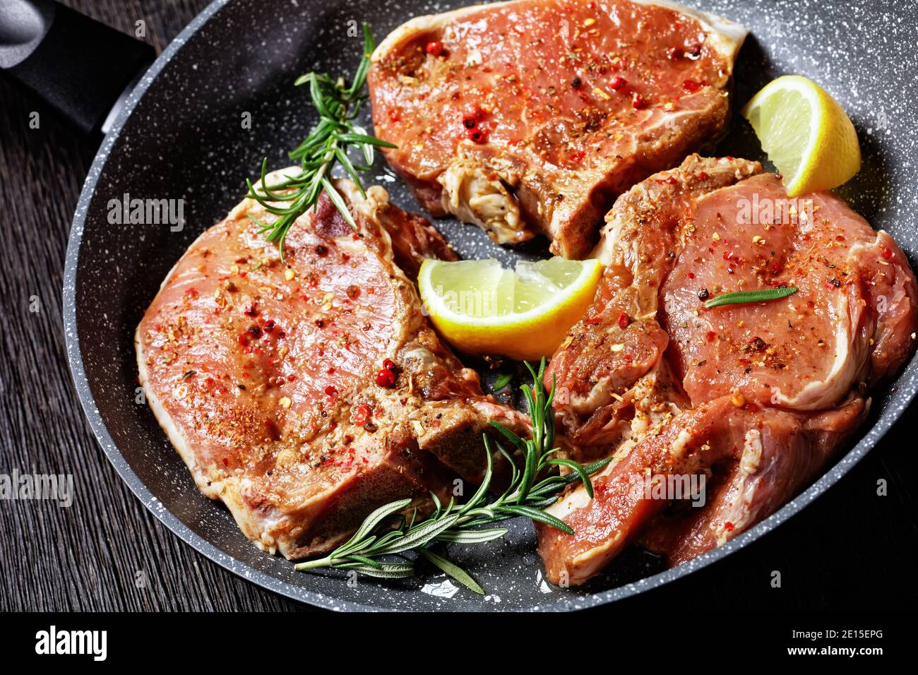 gros plan de côtelettes de porc épicées crues avec des brins de romarin dans une poêle sur une table en bois, vue horizontale d'en haut Banque D'Images