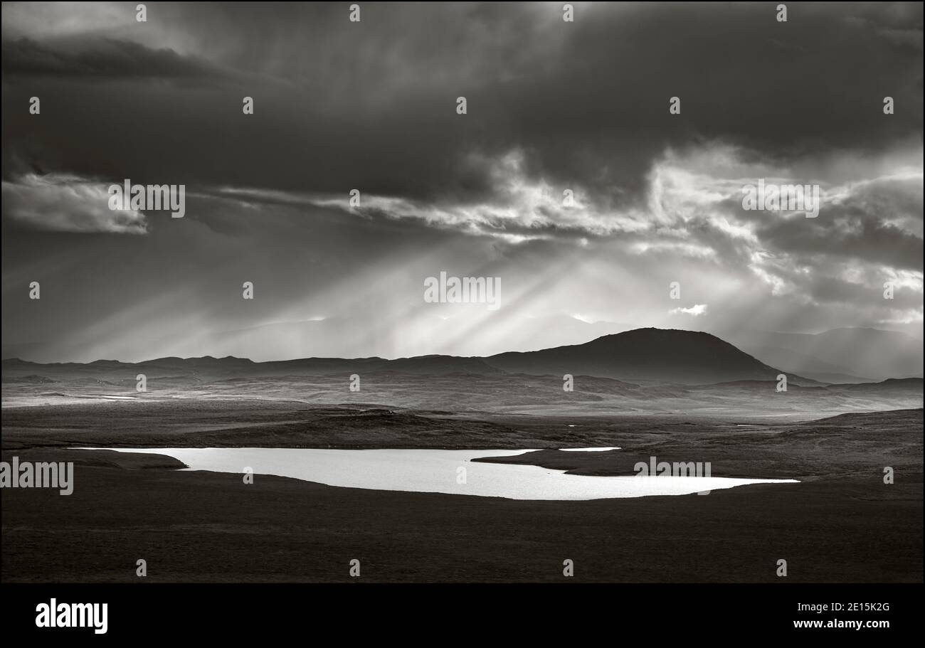 Écosse, Île de Lewis et Harris : approche de nuages de tempête avec des rayons du soleil et des réflexions sur un petit lac Banque D'Images