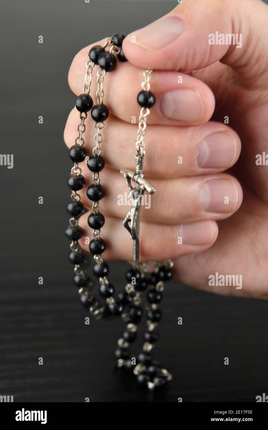 Main de l'homme priant les perles de Rosaire avec le crucifix Banque D'Images