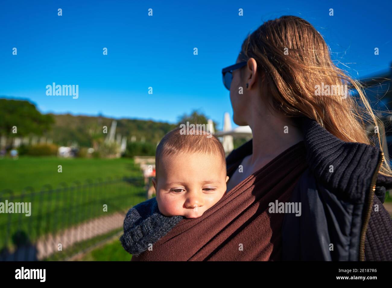 Une jeune mère est dans le parc avec son bébé dans une anse à bande le jour d'automne ensoleillé Banque D'Images