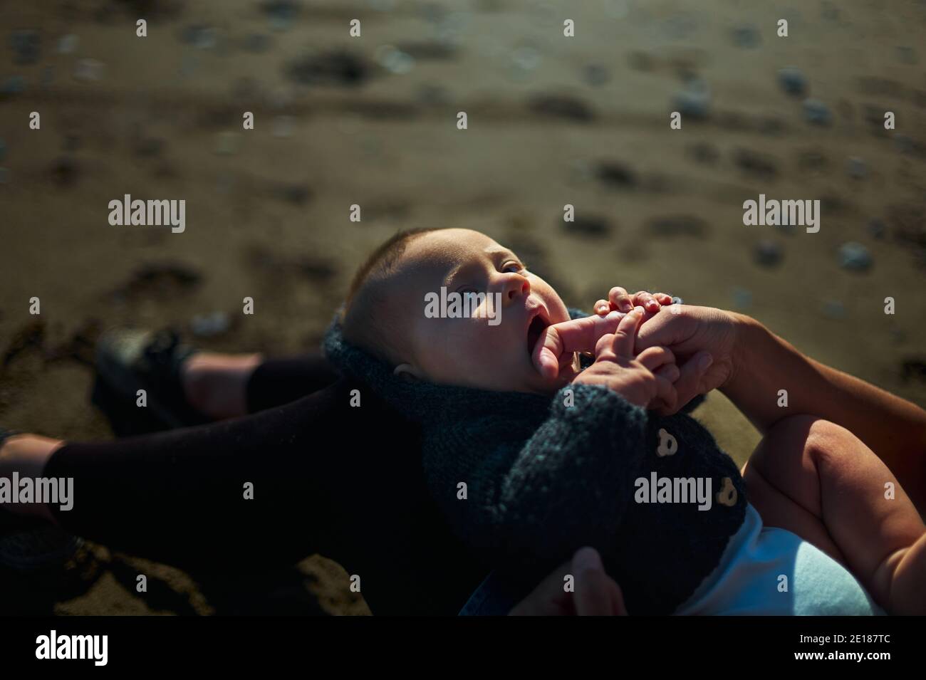 Un petit bébé se repose sur les genoux de ses mères la plage le jour d'automne ensoleillé Banque D'Images