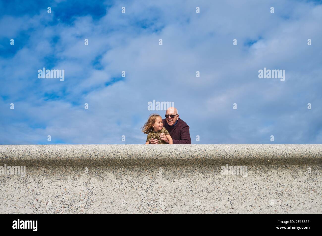 Un pré-chooler repose sur un mur avec son grand-père en été Banque D'Images