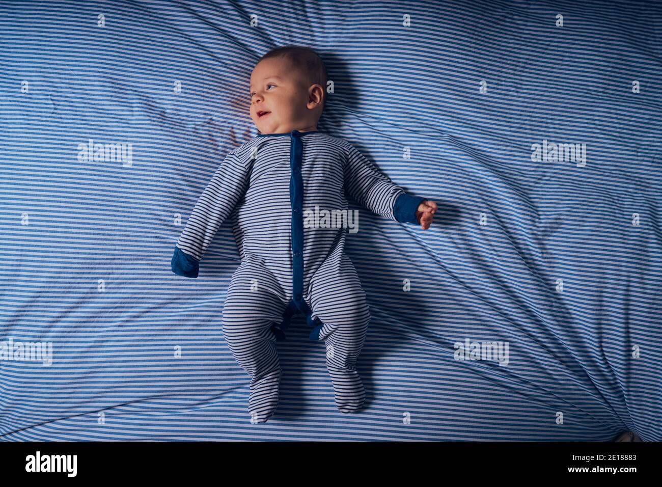 Un petit bébé dans une barboteuse rayée est couché lit assorti Banque D'Images