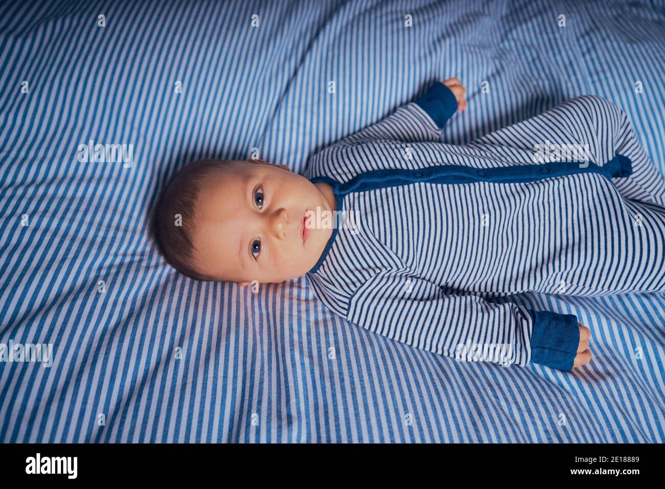 Un petit bébé dans une barboteuse rayée est couché lit assorti Banque D'Images