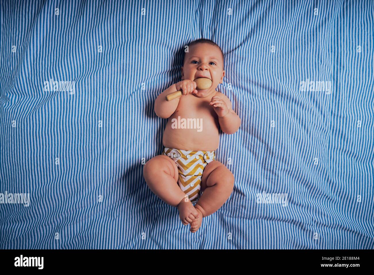 Un petit bébé est allongé sur un lit avec h. un hochet en bois Banque D'Images