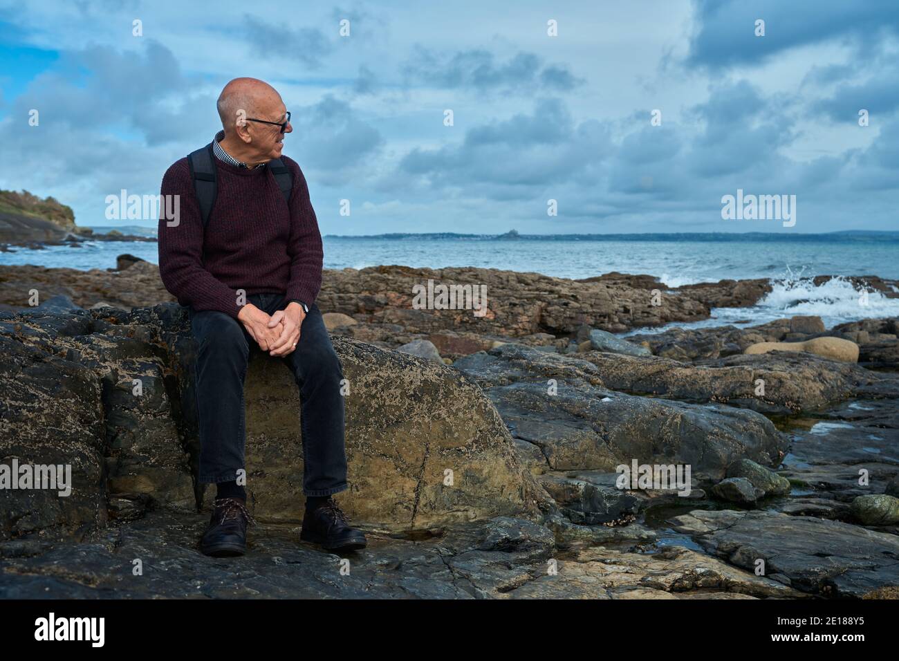 Un homme âgé est assis sur un rocher près du mer en automne Banque D'Images