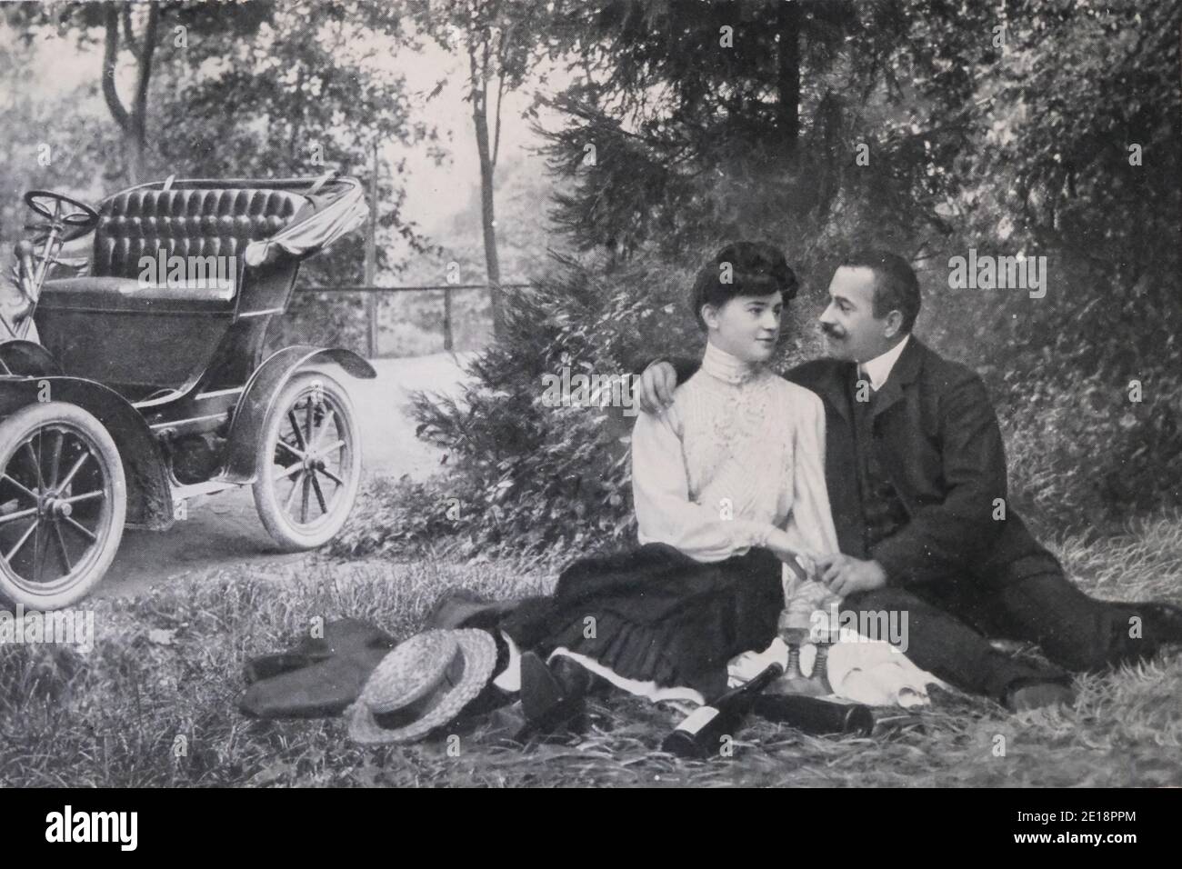 Image vintage en noir et blanc de jeunes amoureux avec voiture, vin et verres en 1907 Banque D'Images