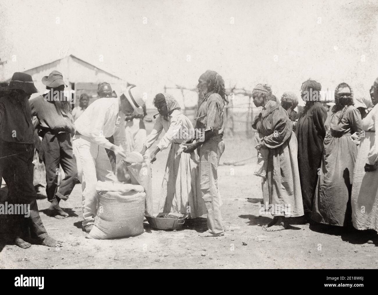 Photographie vintage du début du XXe siècle - autochtones recevant des rations d'un groupe d'hommes blancs, Australie, vers 1910. Banque D'Images