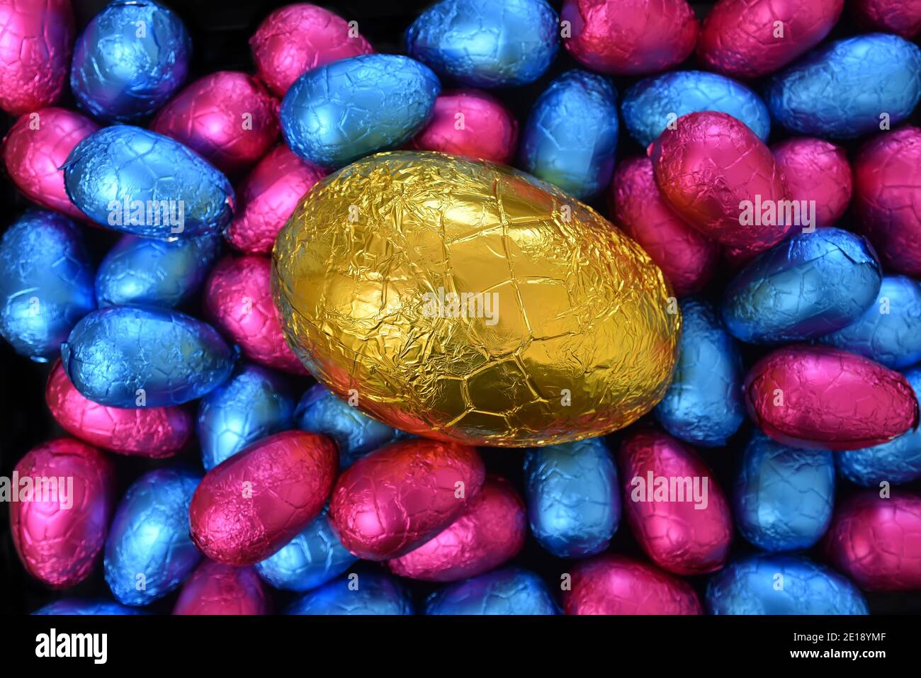 Pile ou groupe de plusieurs couleurs et de différentes tailles de papier d'aluminium coloré enveloppé chocolat oeufs de pâques en rose, et bleu, avec un gros oeuf jaune d'or dans Banque D'Images