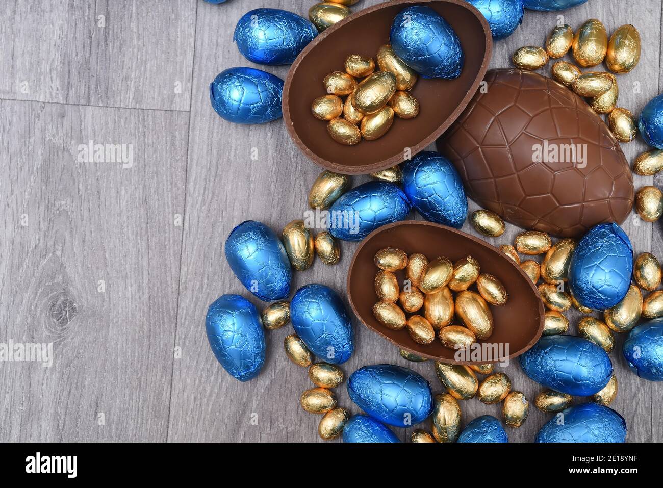 Pile ou groupe de différentes tailles d'oeufs de pâques au chocolat enveloppés de papier d'aluminium coloré en bleu et or. Les grandes moitiés d'un œuf au chocolat au lait brun ont des mi Banque D'Images