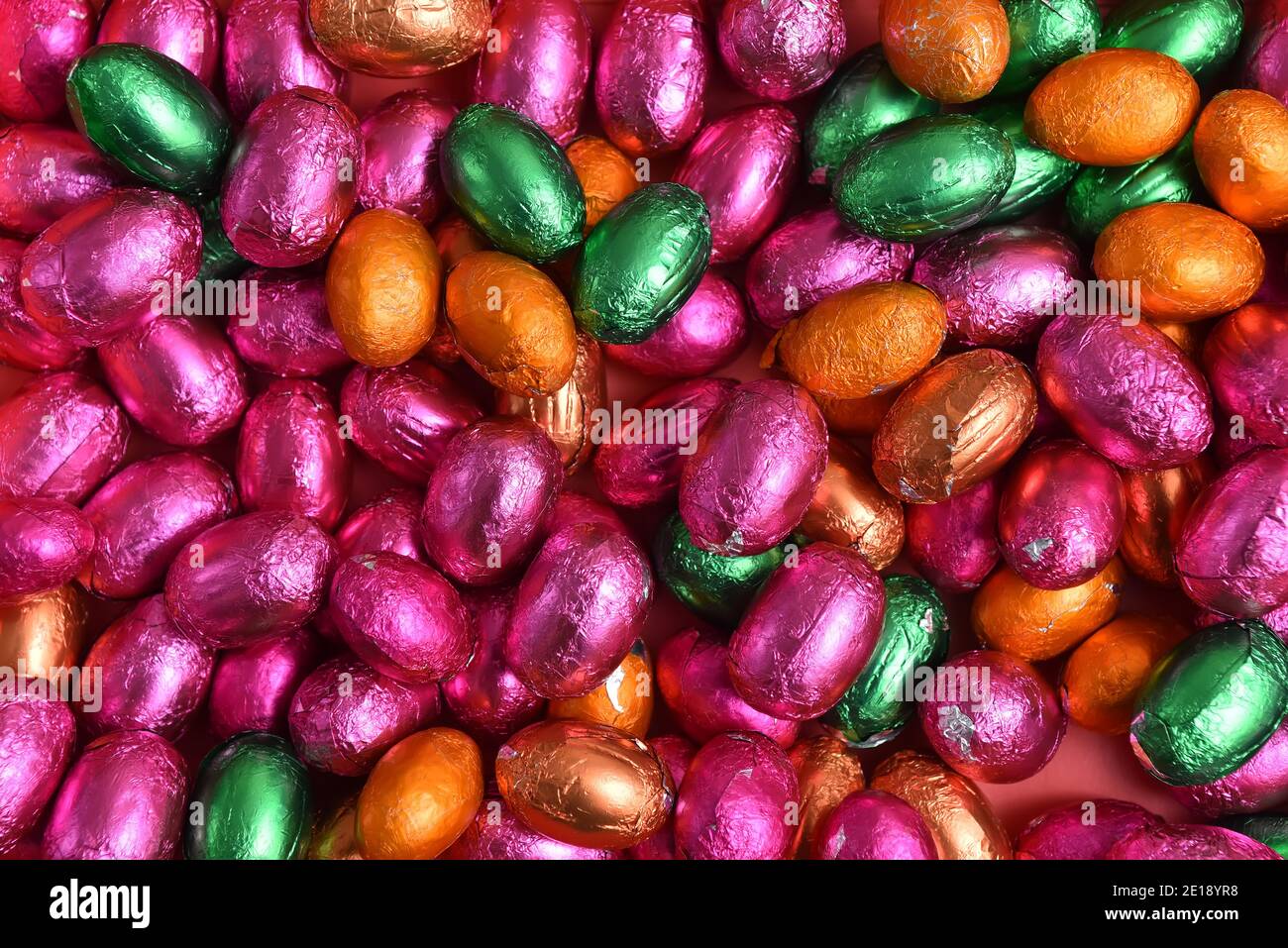 Petits et grands œufs de pâques en papier d'aluminium rose, vert, orange et bronze, sur fond orange pêche. Banque D'Images