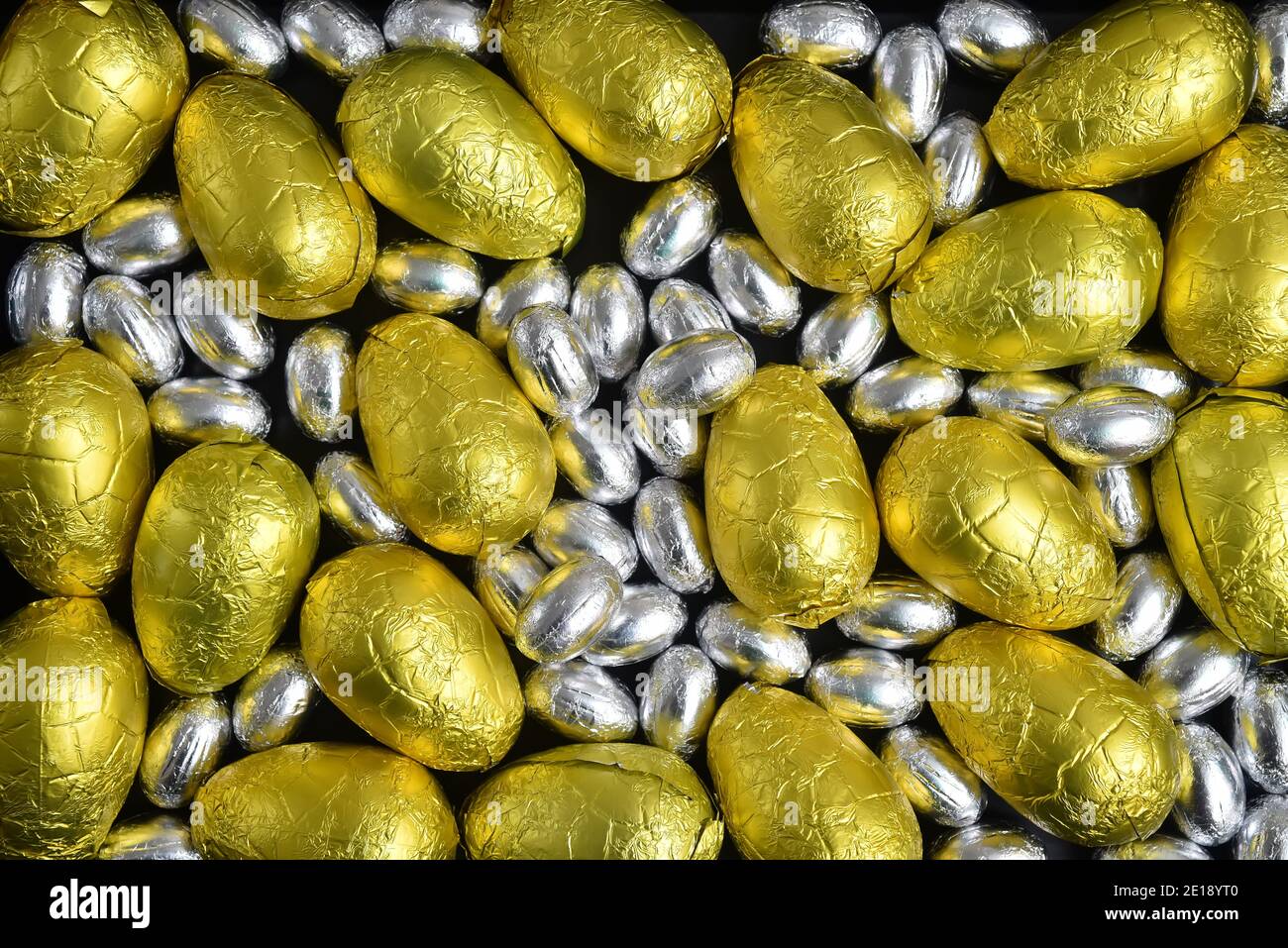 Petits et grands œufs de pâques en papier d'aluminium jaune, or et argent, sur fond noir. Banque D'Images