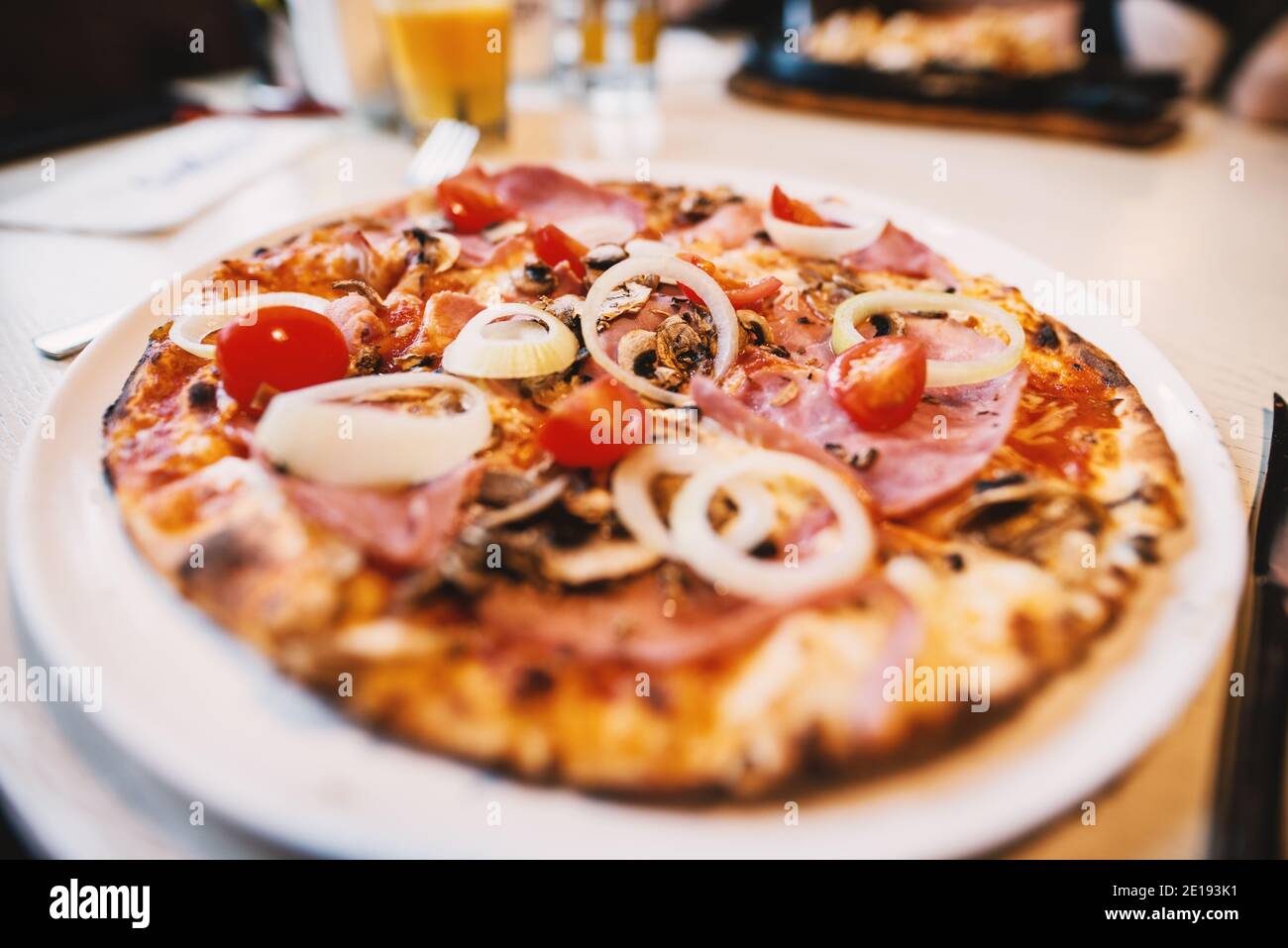 Une délicieuse pizza avec des tomates et des oignons sur la plaque blanche du restaurant pendant que les amis déjeunent. Banque D'Images