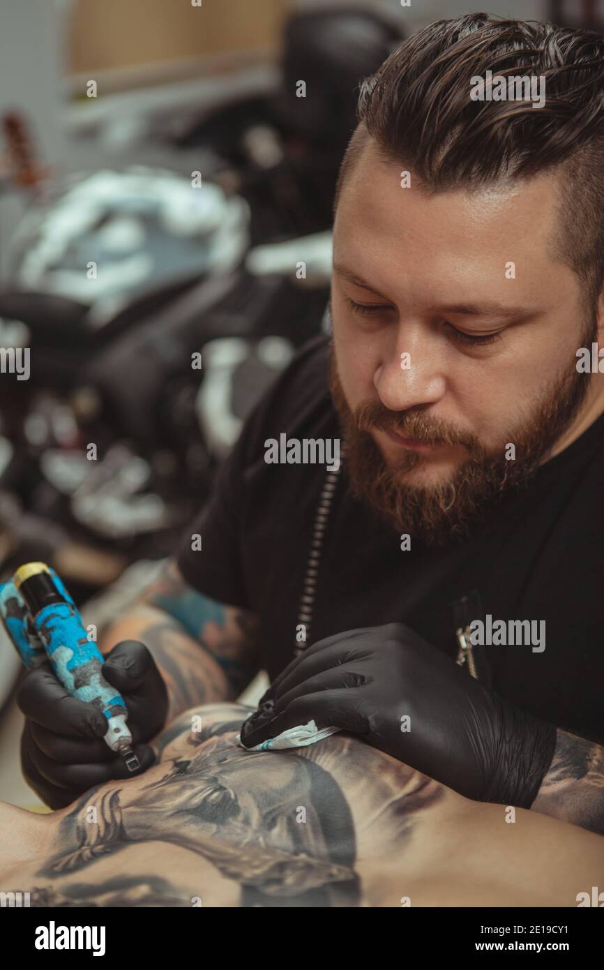 Photo verticale d'un tatoo professionnel barbu se concentrant, tout en travaillant dans son studio. Photo rognée d'un tatouage dessinant un tatouage sur la poitrine o Banque D'Images