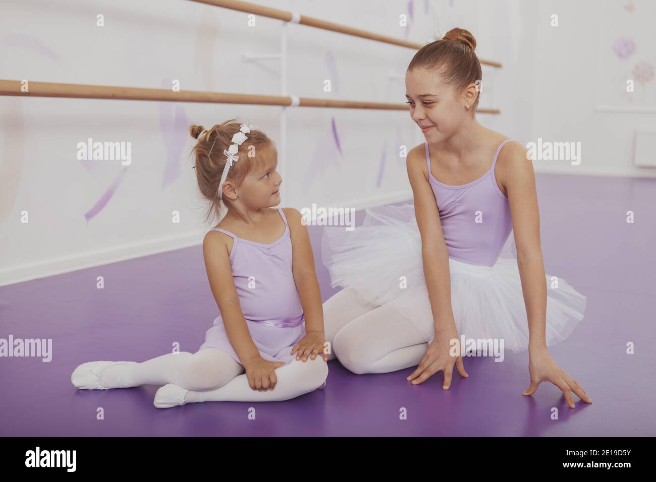 Deux jeunes ballerines adorables souriant l'un à l'autre, se reposant sur le  sol après avoir dansé à l'école de ballet. Adorable petite ballerine et sa  sœur lasi Photo Stock - Alamy
