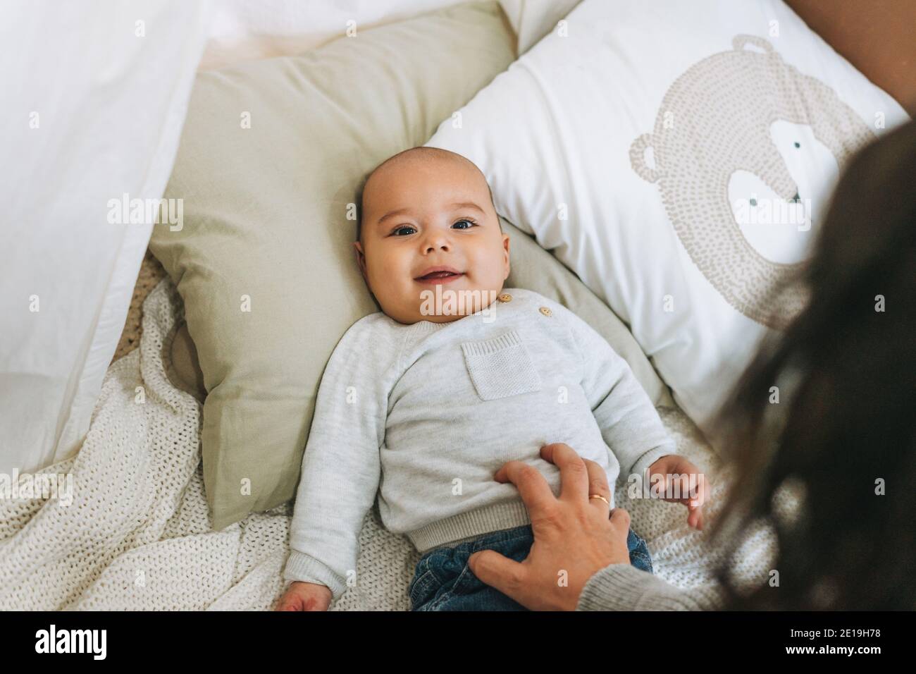 Mignon sourire bébé garçon en beige 5-6 mois regarder appareil photo avec mère sur le lit avec couverture tricotée Banque D'Images