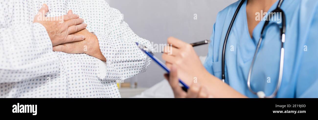 vue rognée d'une femme âgée touchant la poitrine tout en souffrant d'une attaque à l'essence près d'une infirmière écrivant sur un presse-papiers, un premier plan flou, une bannière Banque D'Images