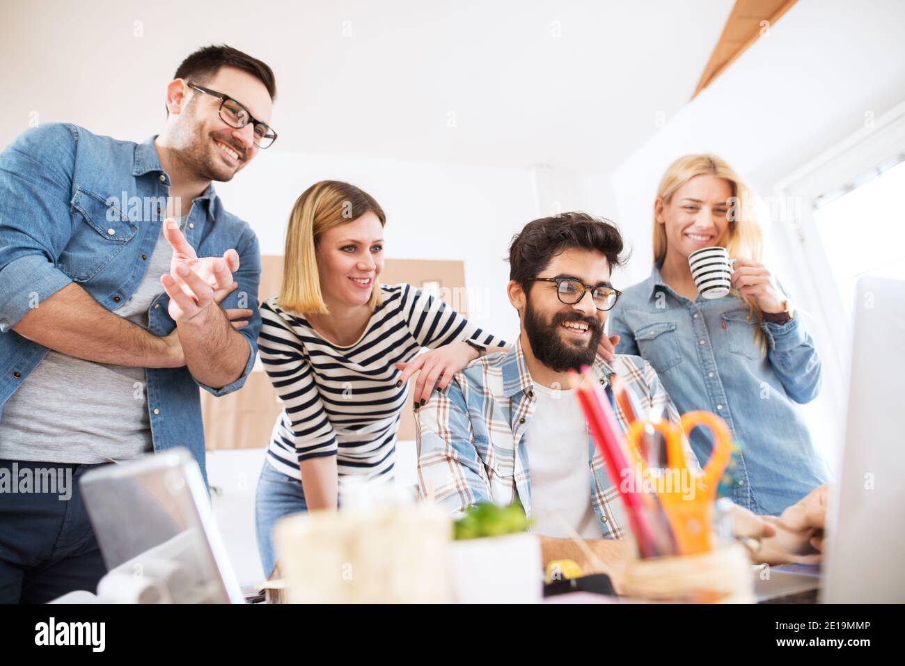 Un groupe de quatre jeunes a satisfait les gens d'affaires qui ont regardé le produit final sur un ordinateur portable au bureau avec plaisir. Banque D'Images