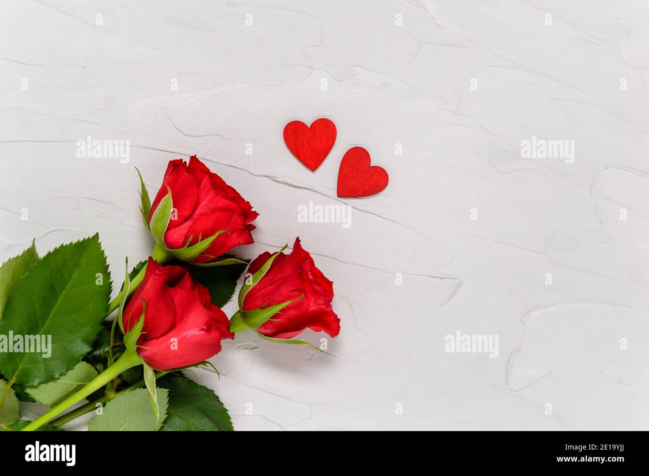 Roses rouges et deux coeurs en bois sur fond de béton texturé par le dessus. Concept d'amour et de convivialité. Saint-Valentin, Fête des mères. Pose à plat Banque D'Images