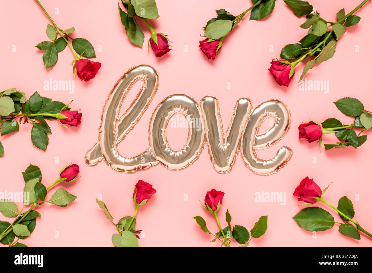 Mot d'amour fait avec la forme brillante de bulle d'aluminium doré entouré de roses rouges sur fond rose. Fête des mères, fête de la Saint-Valentin ou mariage Banque D'Images