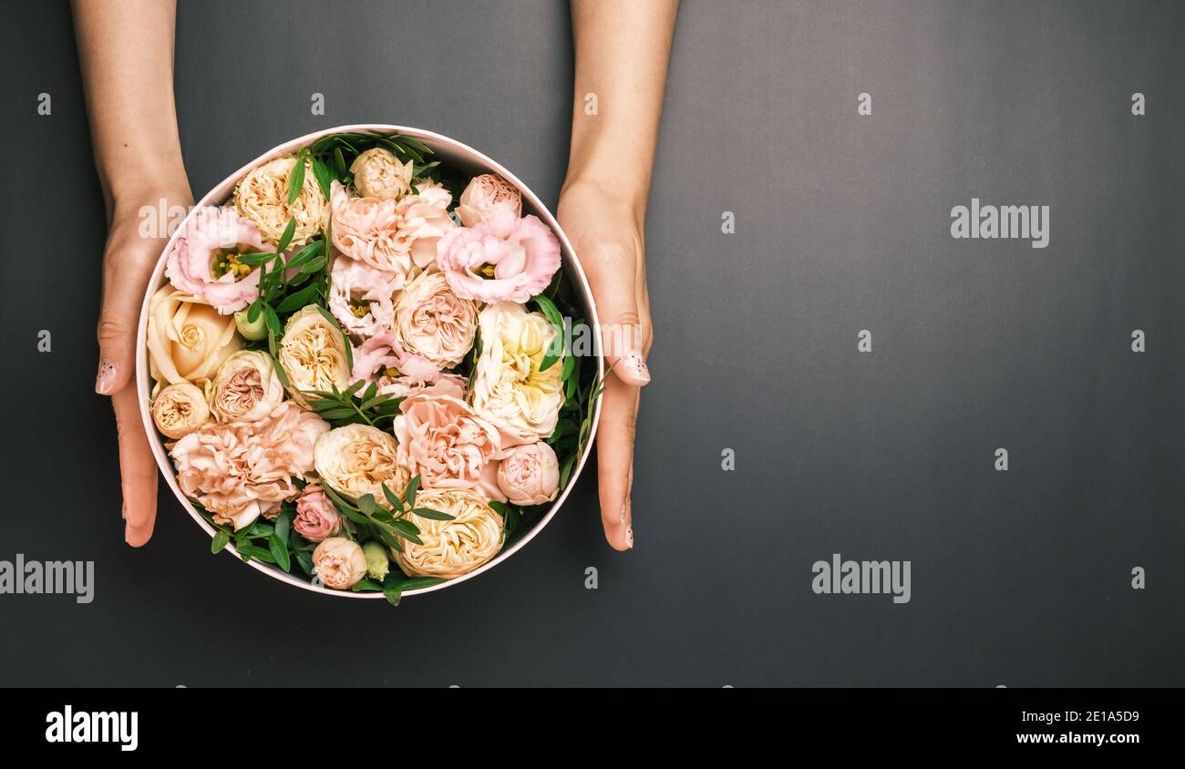 Boîte cadeau rose avec composition florale dans les mains des femmes sur le fond noir avec espace de copie. Cadeau pour la Saint-Valentin, International Women's Banque D'Images