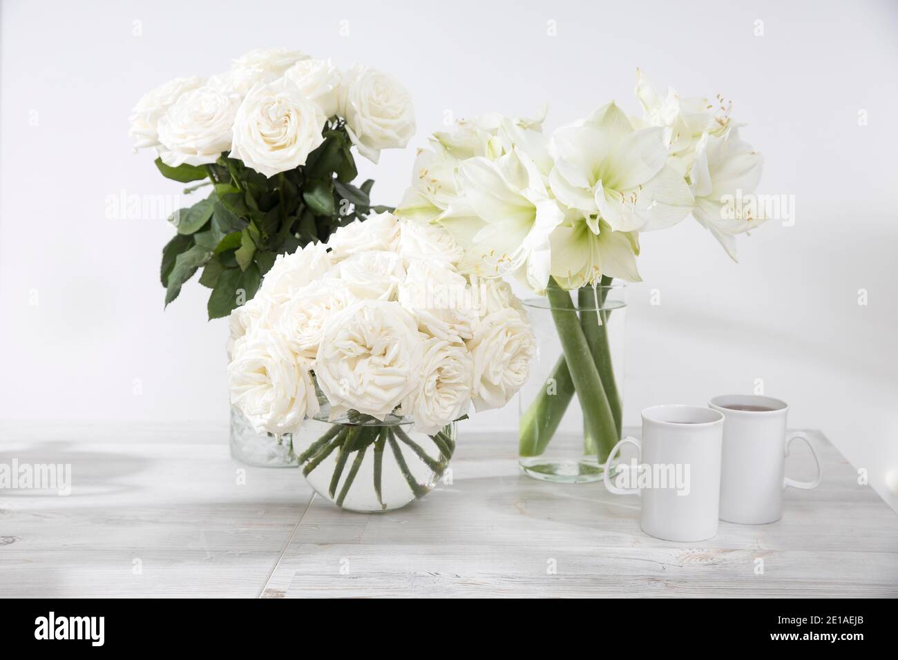 Roses blanches, nénuphars, dans des vases ronds avec deux tasses de café sur la table pour une occasion spéciale comme décoration de cuisine. Copier l'espace Banque D'Images