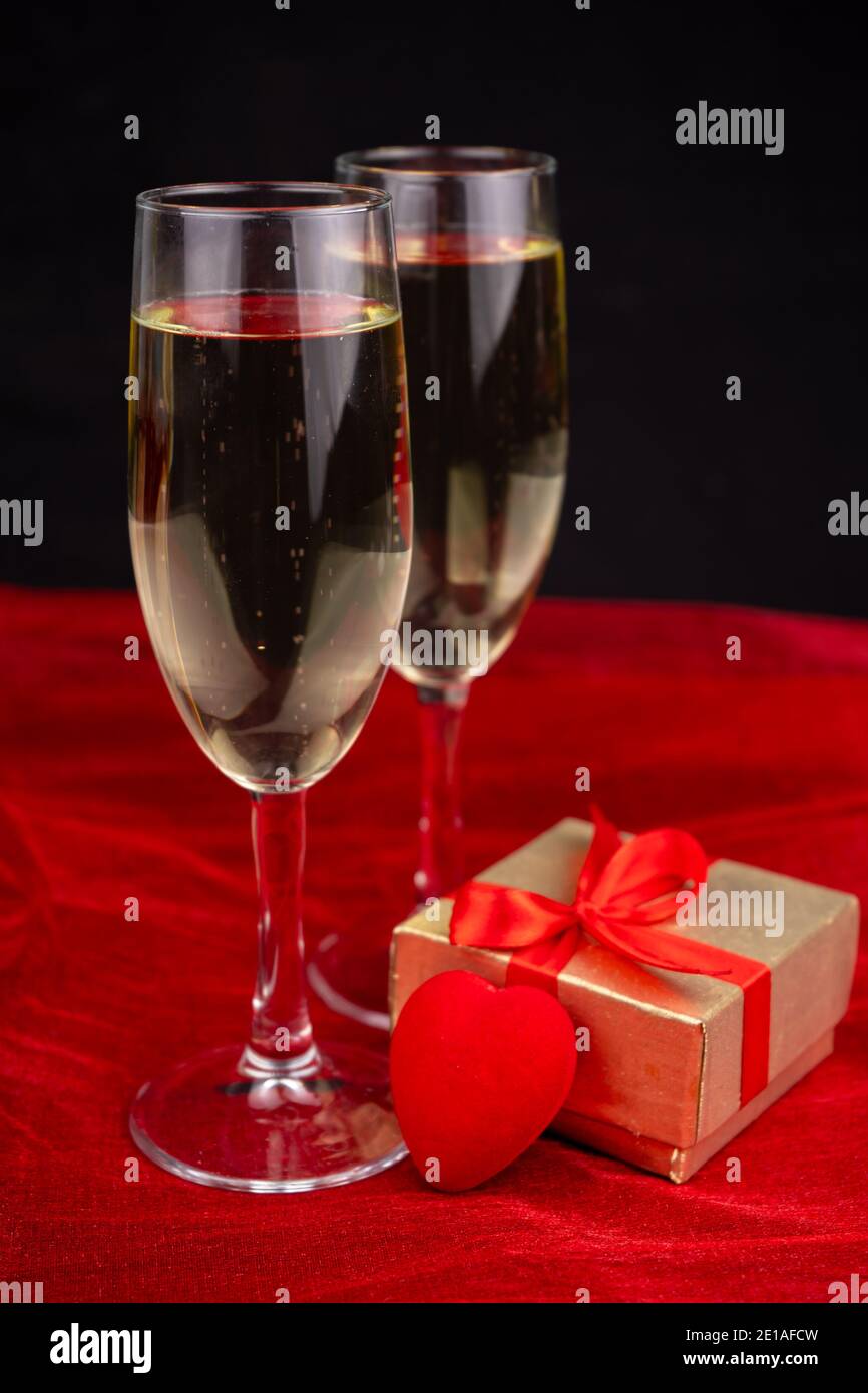 Deux verres avec champagne, boîte cadeau or et décor romantique sur fond noir et rouge Banque D'Images