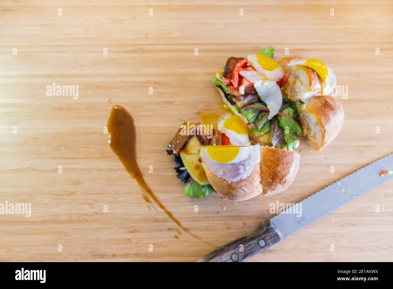 Sandwich complètement farci, coupé en deux, avec des œufs de caille frits et des feuilles vertes, avec un peu de sauce coulée sur le côté, un couteau à découper est placé à côté Banque D'Images