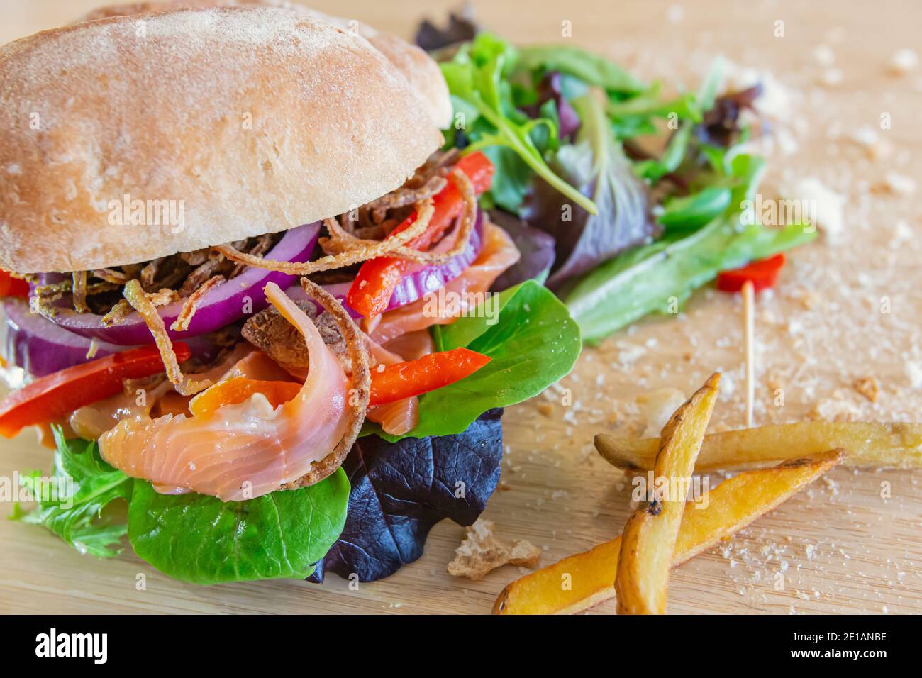 Gros plan d'un sandwich gravelax au saumon, recouvert d'oignons, de tomates et d'autres légumes, placé sur une étagère, avec des miettes et des frites qui l'entourent Banque D'Images