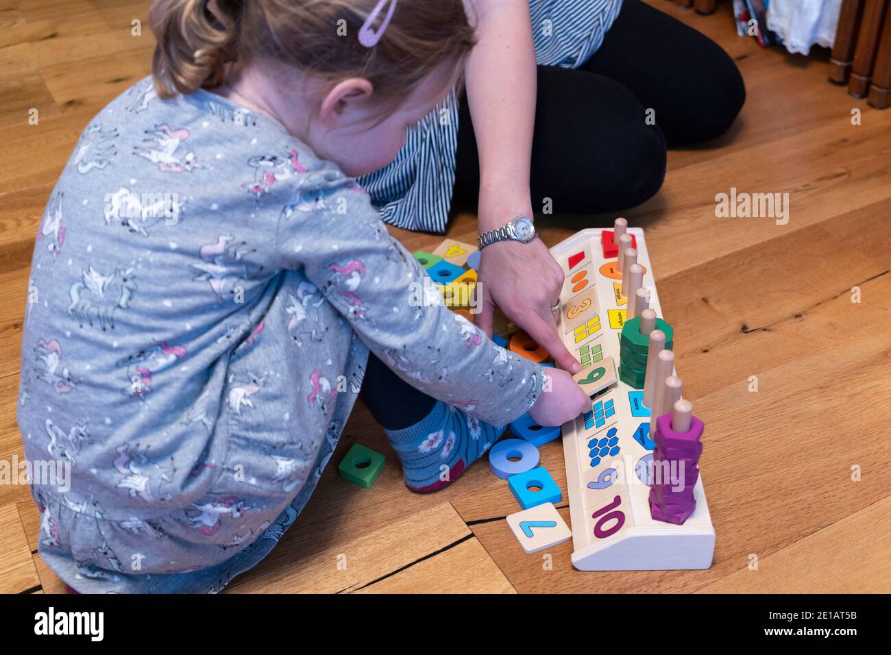 Une mère assise sur le sol et enseignant à sa jeune fille de deux ans à compter avec un comptage en bois forme le jouet éducatif de l'empileur Banque D'Images