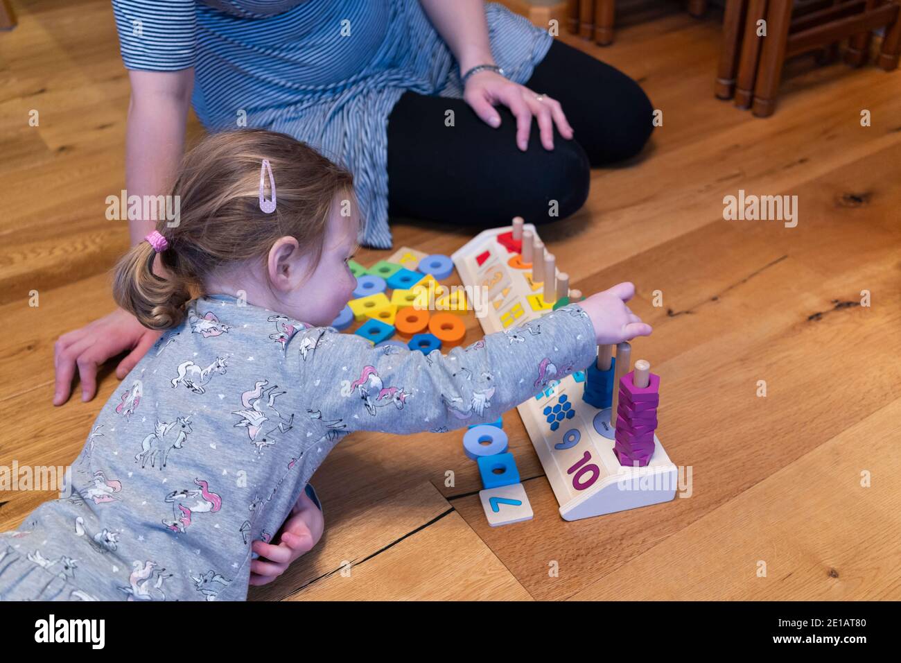 Une mère assise sur le sol et enseignant à sa jeune fille de deux ans à compter avec un comptage en bois forme le jouet éducatif de l'empileur Banque D'Images