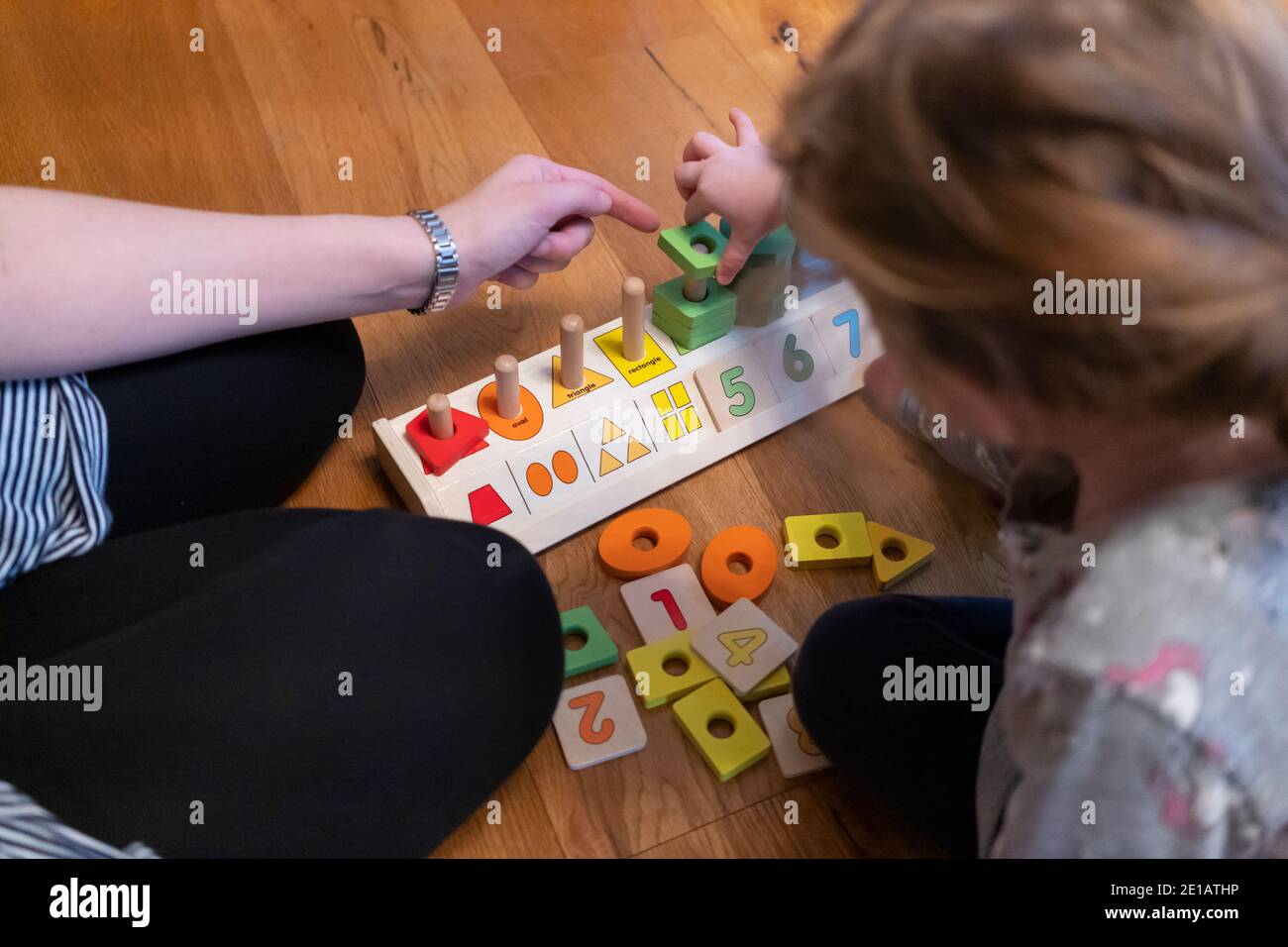 Une mère assise sur le sol et enseignant à sa jeune fille de deux ans à compter en pointant à l'aide d'un jeu éducatif de l'empileur de formes de comptage en bois Banque D'Images