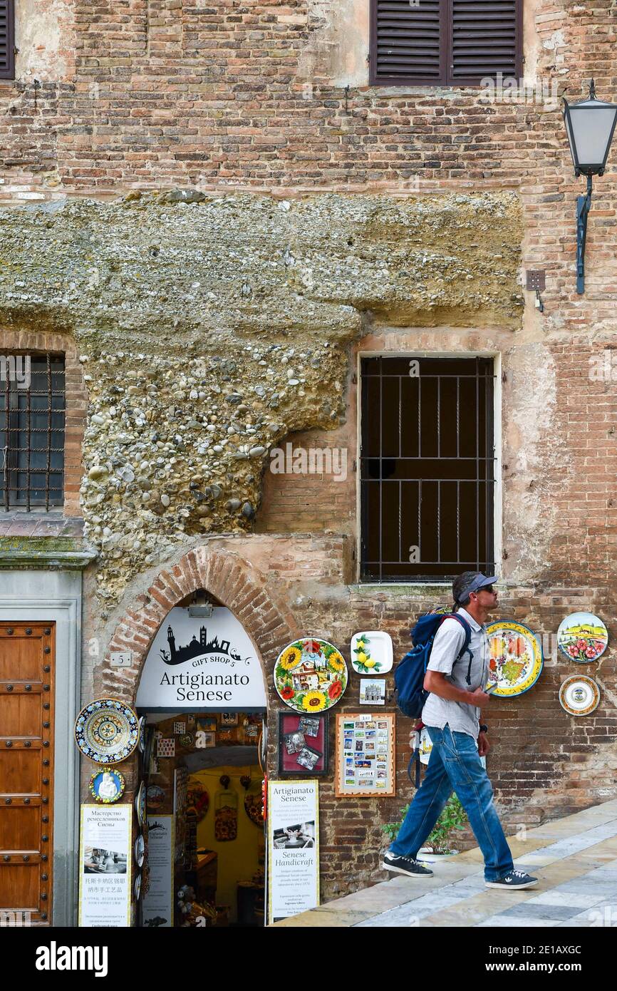 Un touriste avec un sac à dos marche devant un bâtiment médiéval avec une boutique de souvenirs dans le centre historique de Sienne, UNESCO W.H. Site, Toscane, Italie Banque D'Images