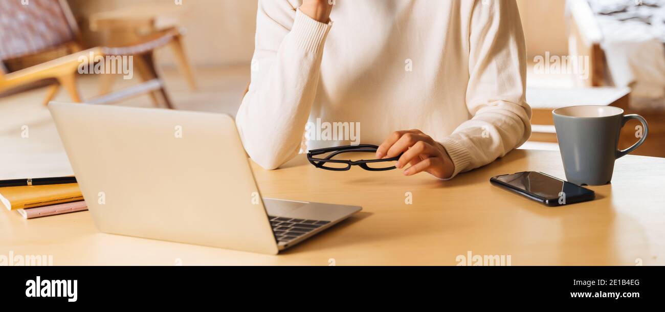 Jeune femme d'affaires asiatique en chandail d'hiver avec des lunettes en utilisant un ordinateur portable souriant. Femme indépendante assise à table et travaillant à domicile. Banque D'Images