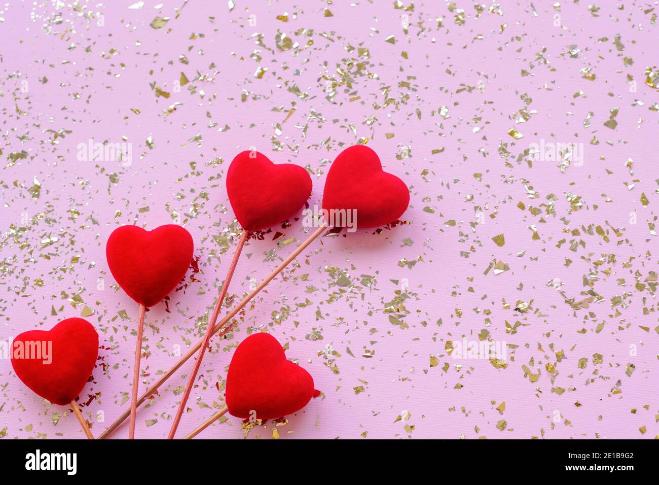 Cinq coeurs rouges sur fond rose festif avec confetti dorés. Concept de la Saint-Valentin. Vue de dessus, plat, espace de copie. Banque D'Images