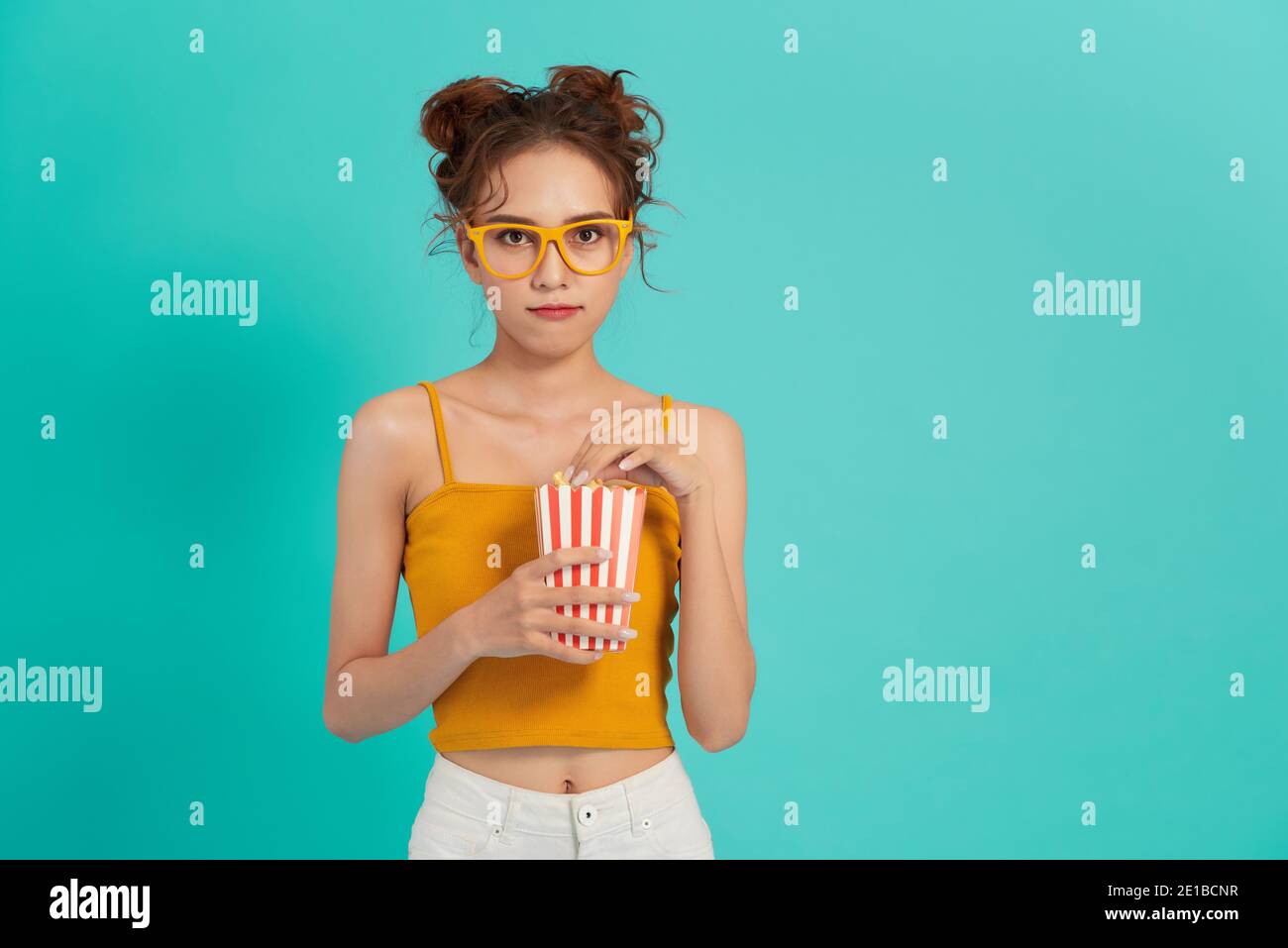 Portrait d'une fille qui rit dans des vêtements décontractés tenant du pop-corn et en regardant la caméra isolée sur un arrière-plan lumineux Banque D'Images